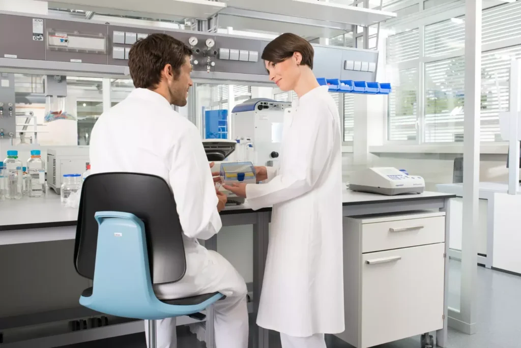 Deux personnes en blouse discutant devant un instrument, l’une assise sur un siège LABSIT bleu