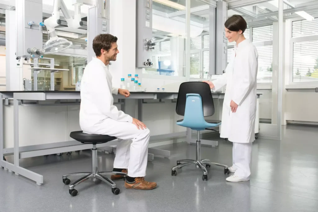 Personne assise sur un tabouret à une paillasse haute à côté d’un siège LABSIT bleu