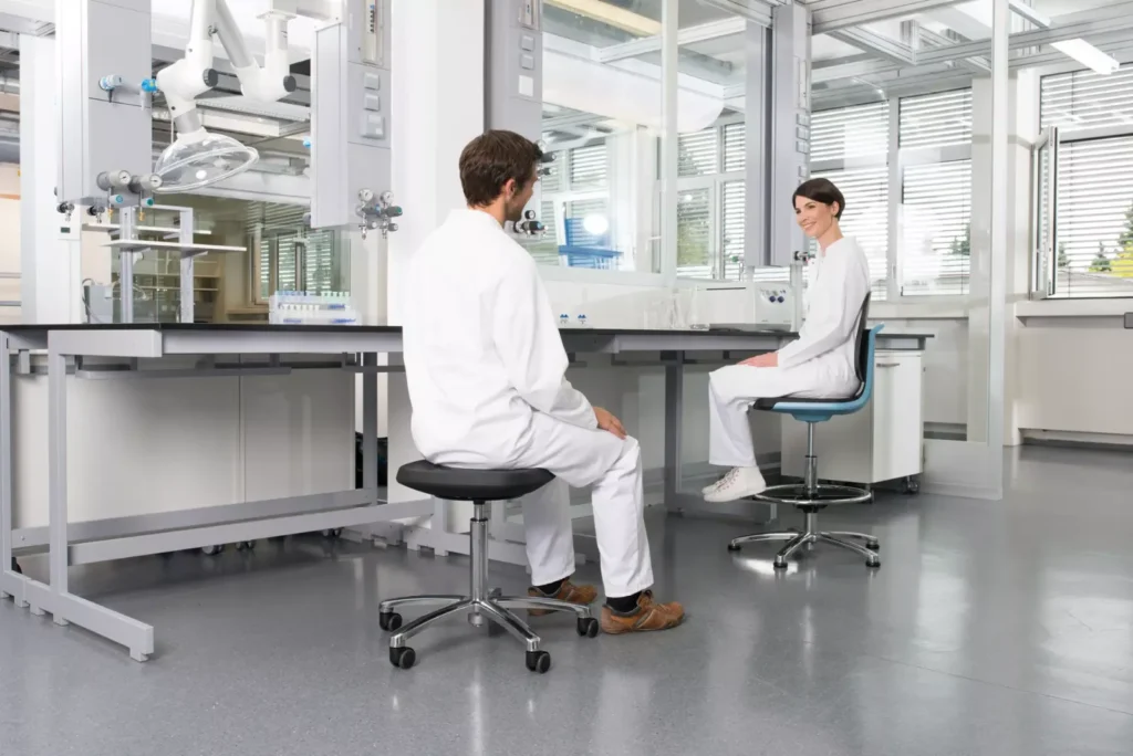 Deux personnes en blouse assises sur un siège LABSIT et un tabouret à une paillasse de laboratoire